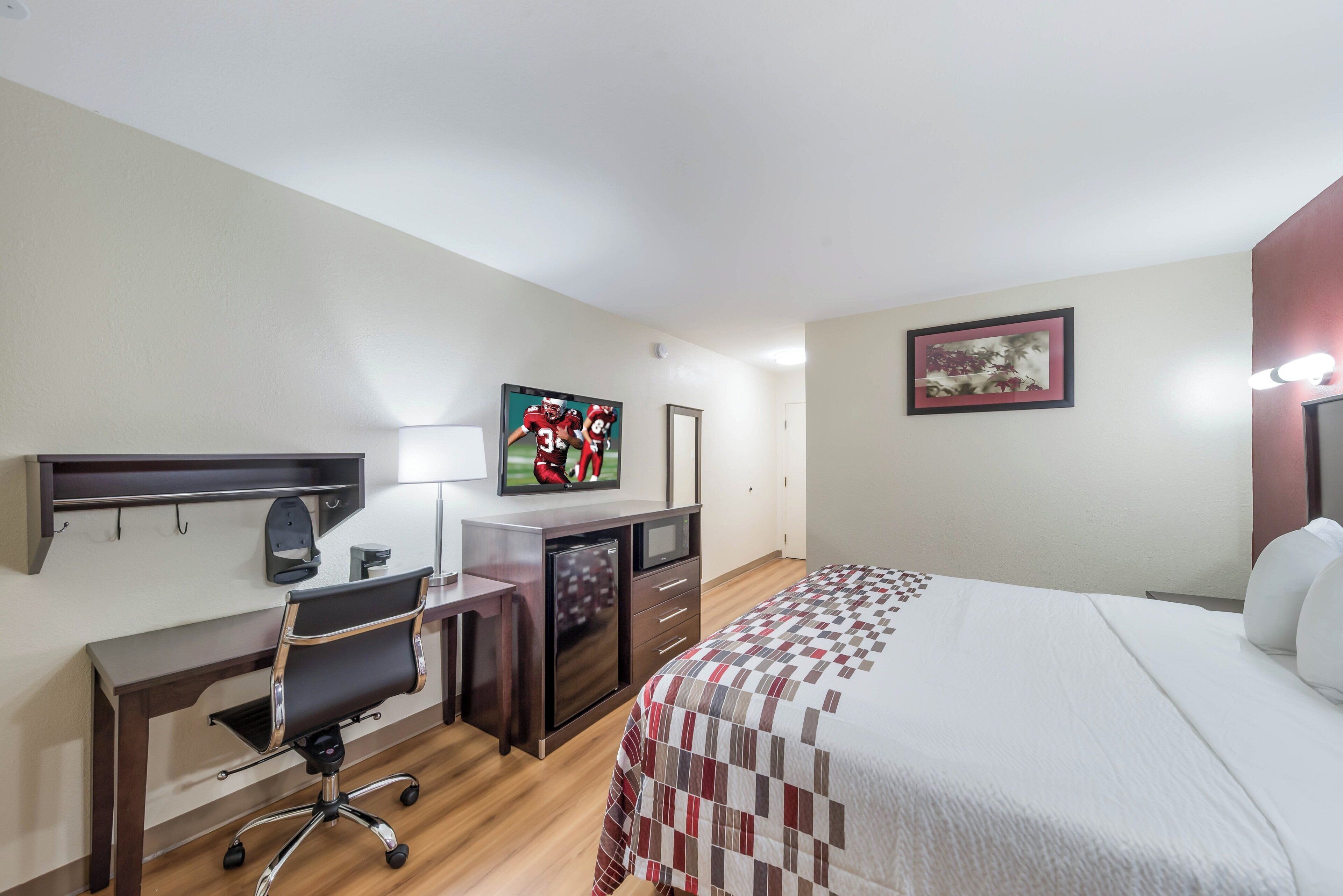 A hotel room with a bed, desk, chair, television, and a framed picture on the wall.