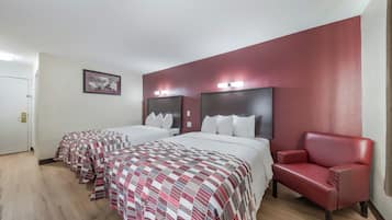 A hotel room with two beds, a red leather chair, and a framed picture on the wall.