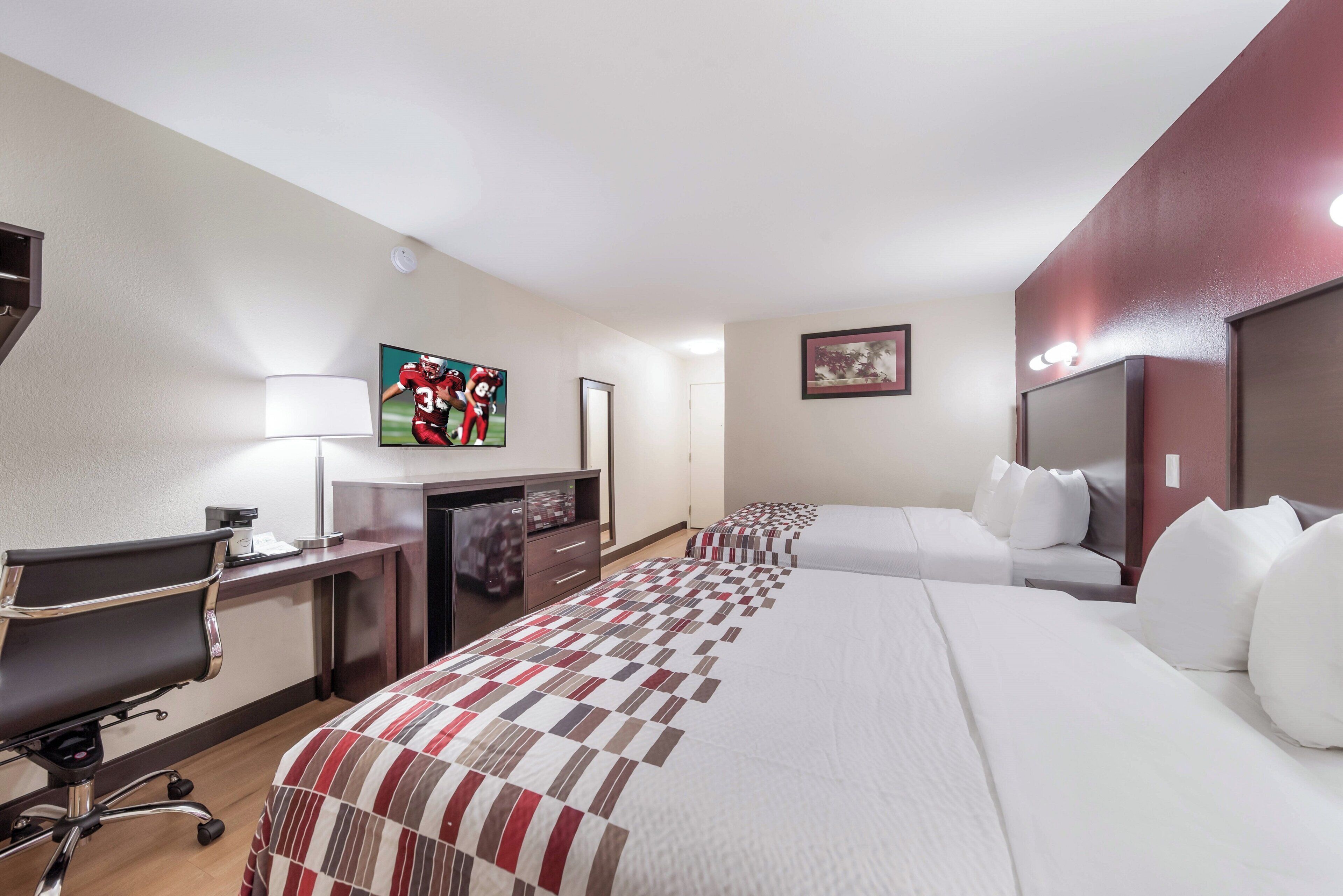 A hotel room with a bed, a desk with a chair, a television, and a painting on the wall.