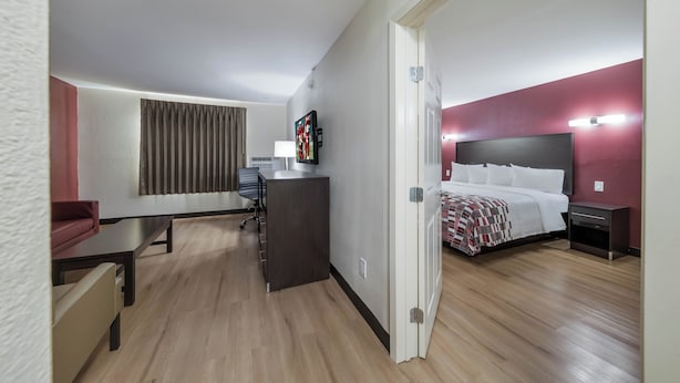 Quarto de hotel com cama, mesa de cabeceira, escrivaninha, cadeira e televisão.