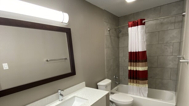 A modern bathroom with a large mirror, a sink, toilet, and a bathtub. - Red Roof Inn & Suites Denton (Denton)