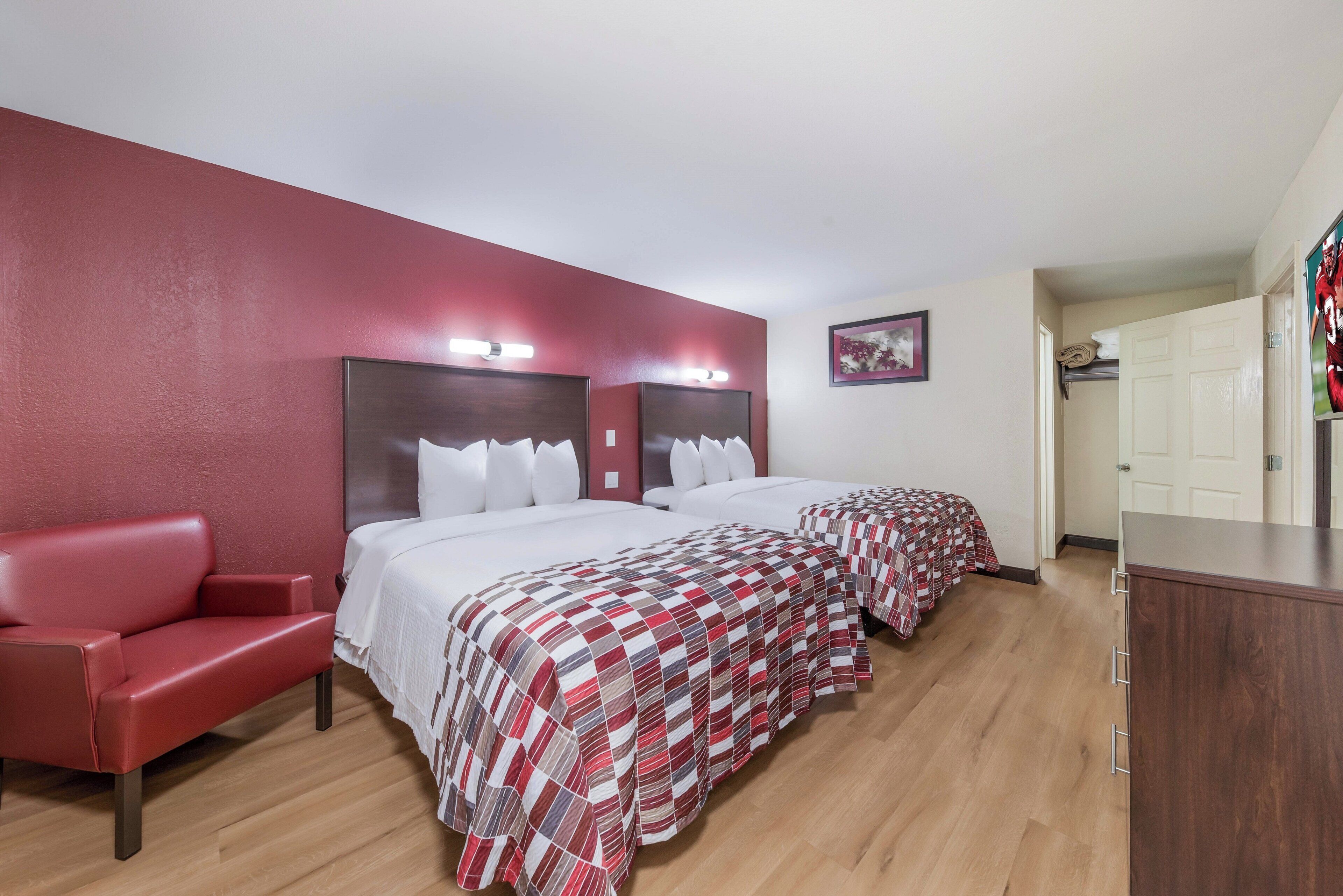 A hotel room with two beds, a red armchair, and a wooden floor.