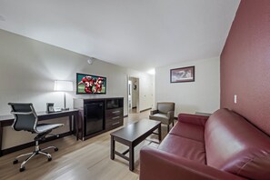 A modern living room with a flat-screen TV, a desk with a chair, a sofa, and a coffee table. - Red Roof Inn & Suites Denton (Denton)