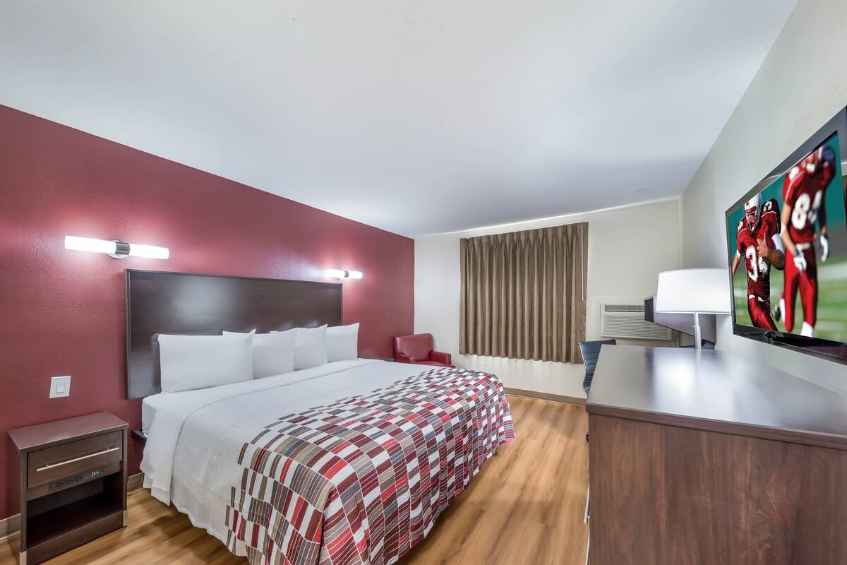 A hotel room with a large bed, a desk, a TV, and a red chair.