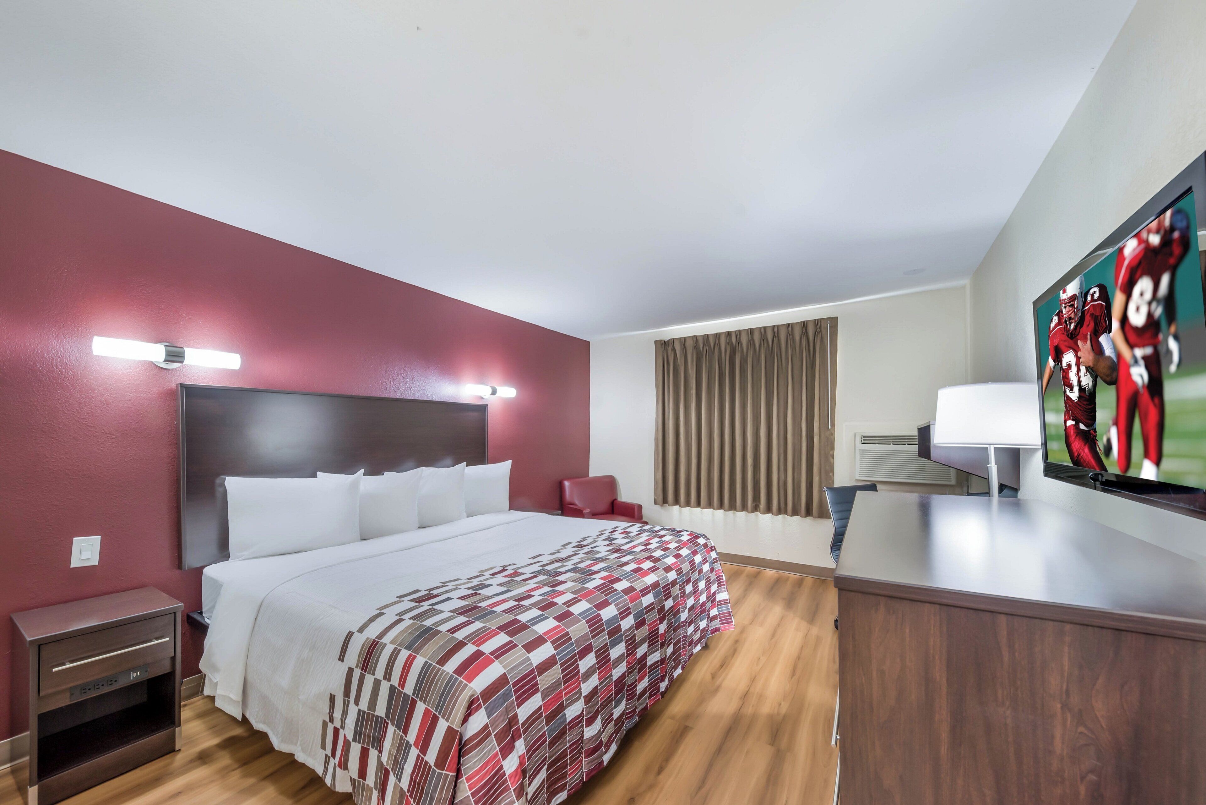 Ein Hotelzimmer mit einem Bett, einem Schreibtisch, einem Sessel, einem Fernseher und einem Fenster mit Vorhängen.