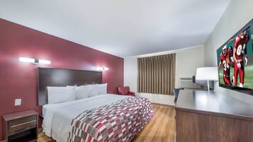 Ein Hotelzimmer mit einem Bett, einem Schreibtisch, einem Sessel, einem Fernseher und einem Fenster mit Vorhängen.
