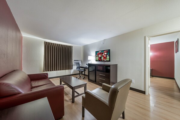 A modern hotel room with a leather sofa, a dining table, a TV, and a desk with a computer. - Red Roof Inn & Suites Denton (Denton)