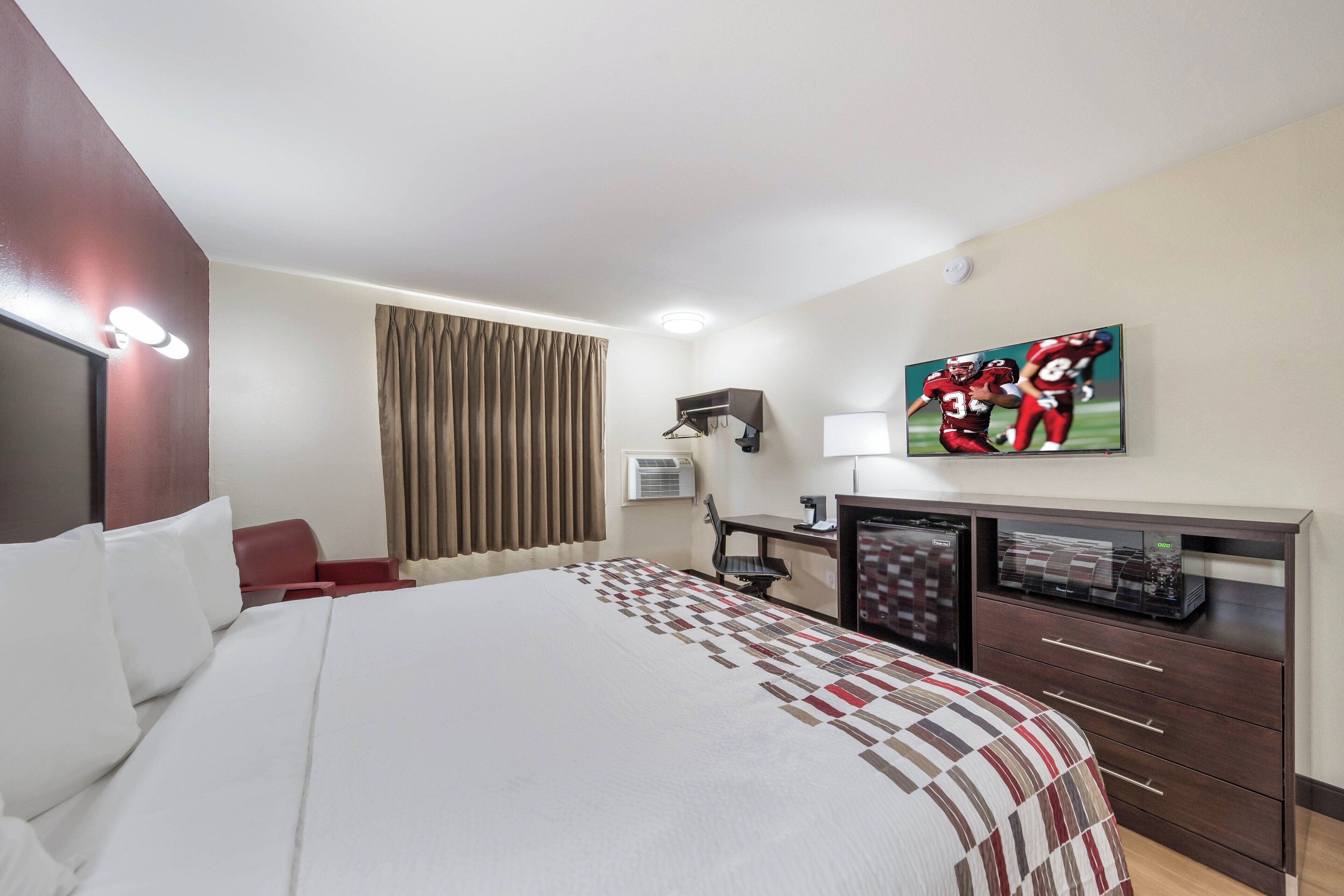 A hotel room with a large bed, a desk with a computer, a flat-screen TV, and a window with curtains.