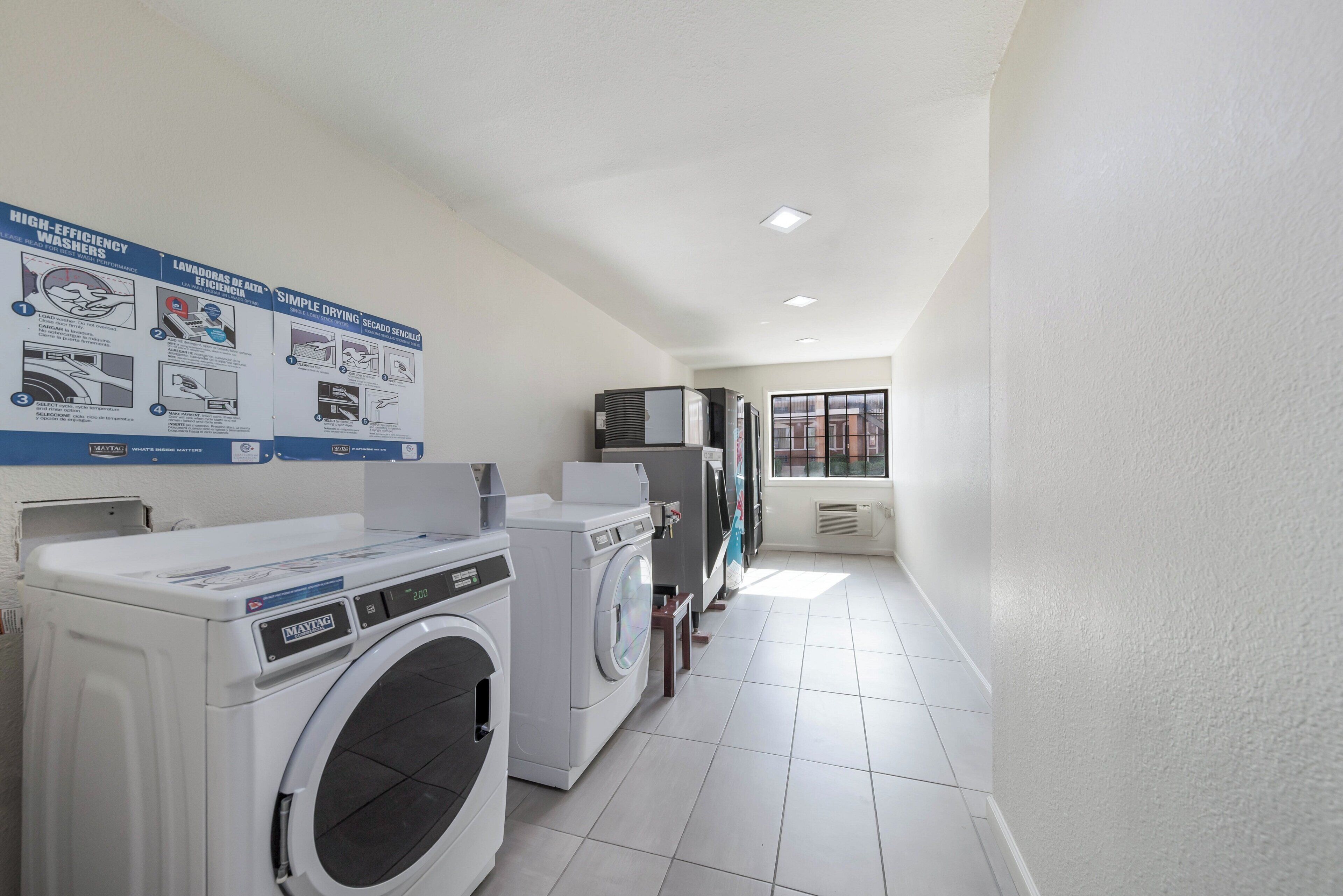 A laundry room with two front-loading washing machines, a dryer, and a wall-mounted instruction poster.