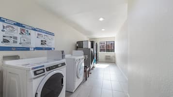 A laundry room with two front-loading washing machines, a dryer, and a wall-mounted instruction poster.