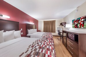 Two single beds with white bedding and a patterned bedspread, a flat-screen TV, and a desk with a chair.