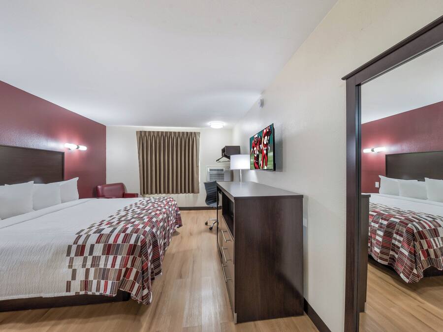 A hotel room with two beds, a desk, a chair, a mirror, and a television.