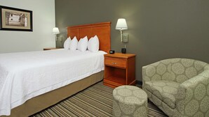 Een hotelkamer met een bed, twee bedlampen, een nachtkastje, een gestreept fauteuil en een vloerbedekking.