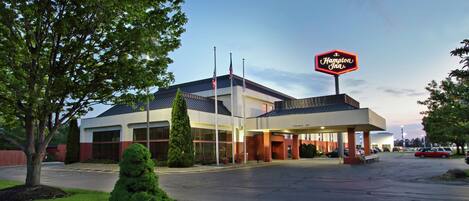 A Hampton Inn with a clear sky, a parking lot, and a well-maintained lawn.