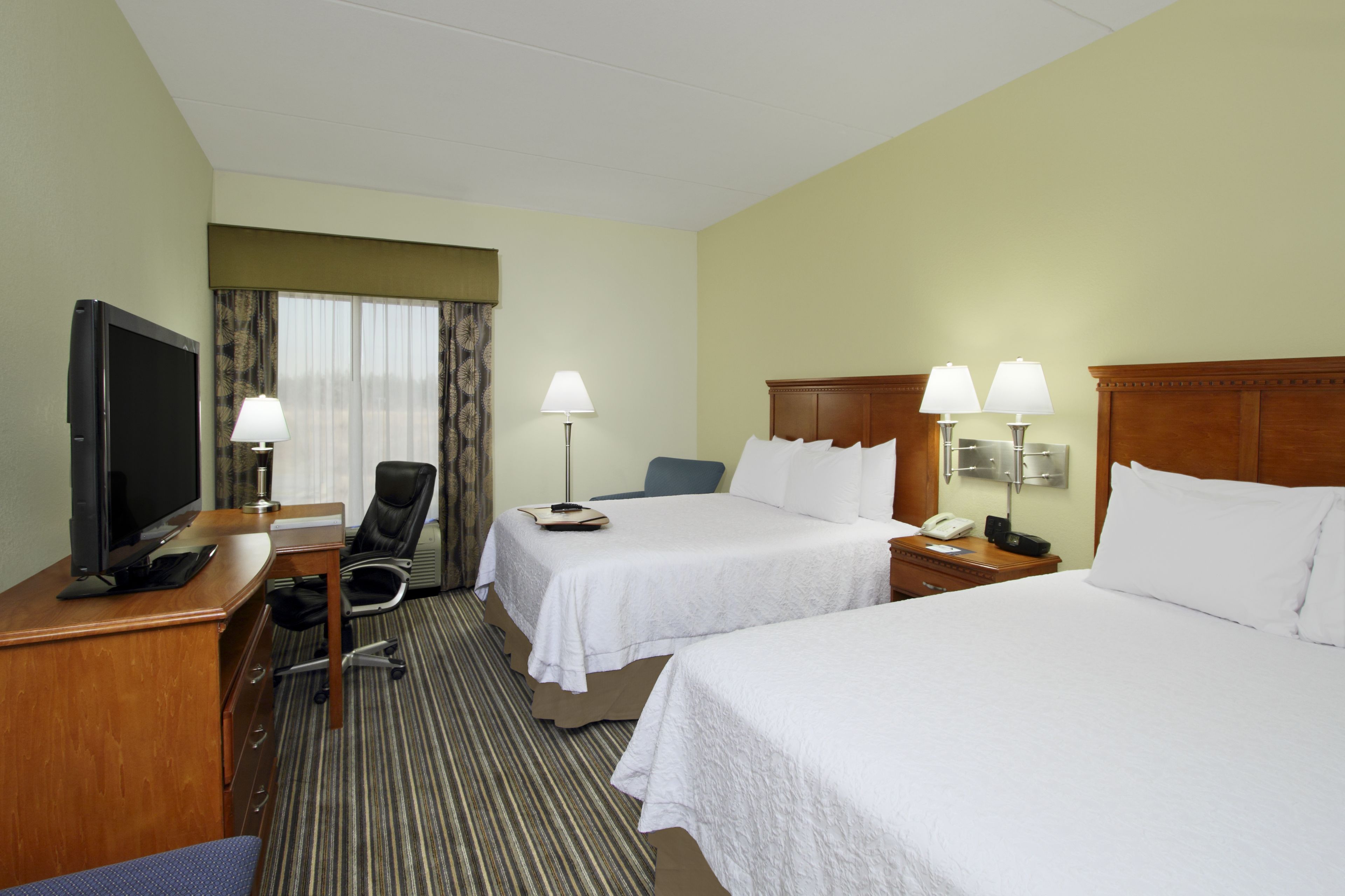 Une chambre d’hôtel avec deux lits, un bureau équipé d’une télévision, une chaise et une lampe.