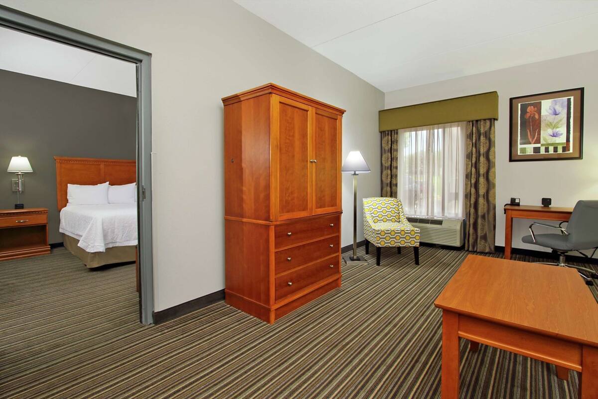 A hotel room with a bed, a wardrobe, a desk, a chair, and a painting on the wall.