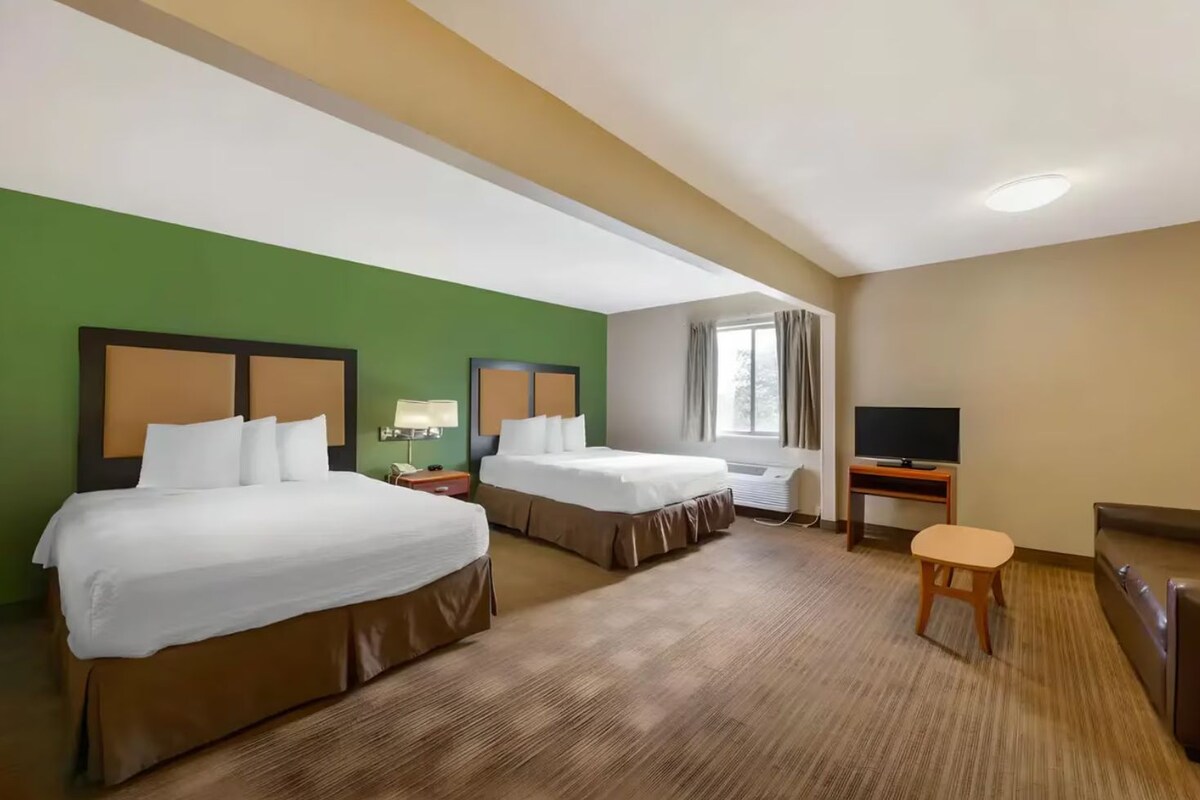 A hotel room with two beds, a TV, a desk, and a window.