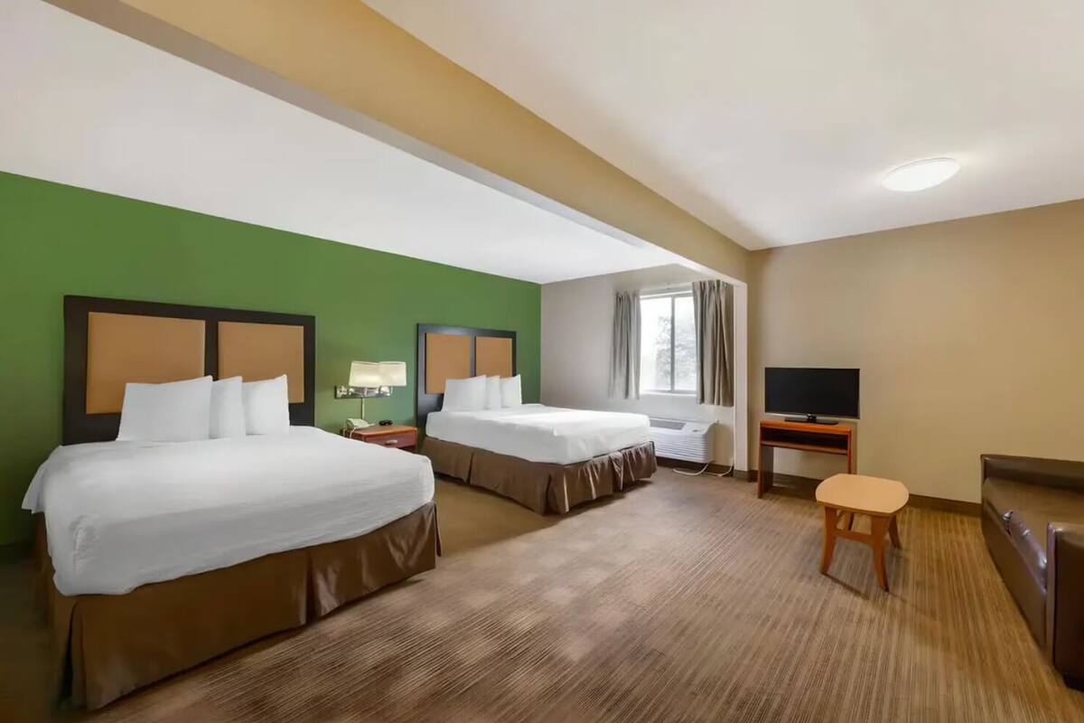 A hotel room with two beds, a TV, a desk, and a window.