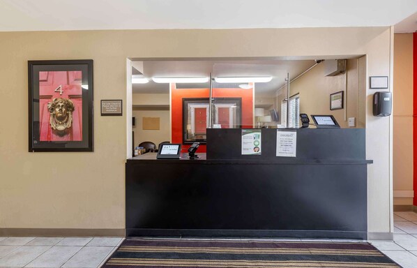 Un mostrador de recepción con una pantalla digital, un cartel enmarcado con el número '4' y una puerta roja al fondo.