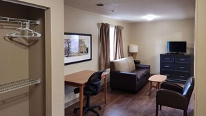 A compact room with a wooden desk, a cushioned chair, a sofa, a small table, a TV, and a dresser. - Suburban Studios Columbus - Dublin (Dublin)