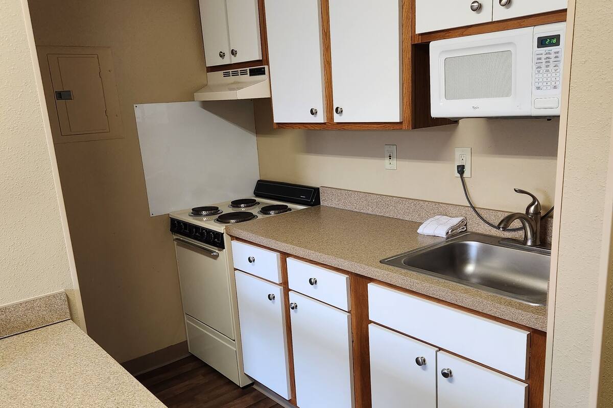 A compact kitchen with white cabinets, a microwave, a stove, and a sink.