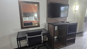 A hotel room with a desk, chair, and a large TV mounted on the wall.