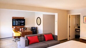 A hotel room with a bed, a sofa with red cushions, a desk with a computer and a coffee maker, and a TV on the wall. - Best Western Cy-Fair (Houston)