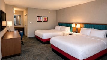 A hotel room with two beds, a desk, a chair, a mirror, and two framed pictures on the wall.
