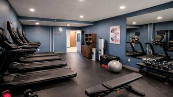 Une salle de sport équipée de tapis de course, d’un banc de musculation, de kettlebells et d’un mur avec des miroirs.