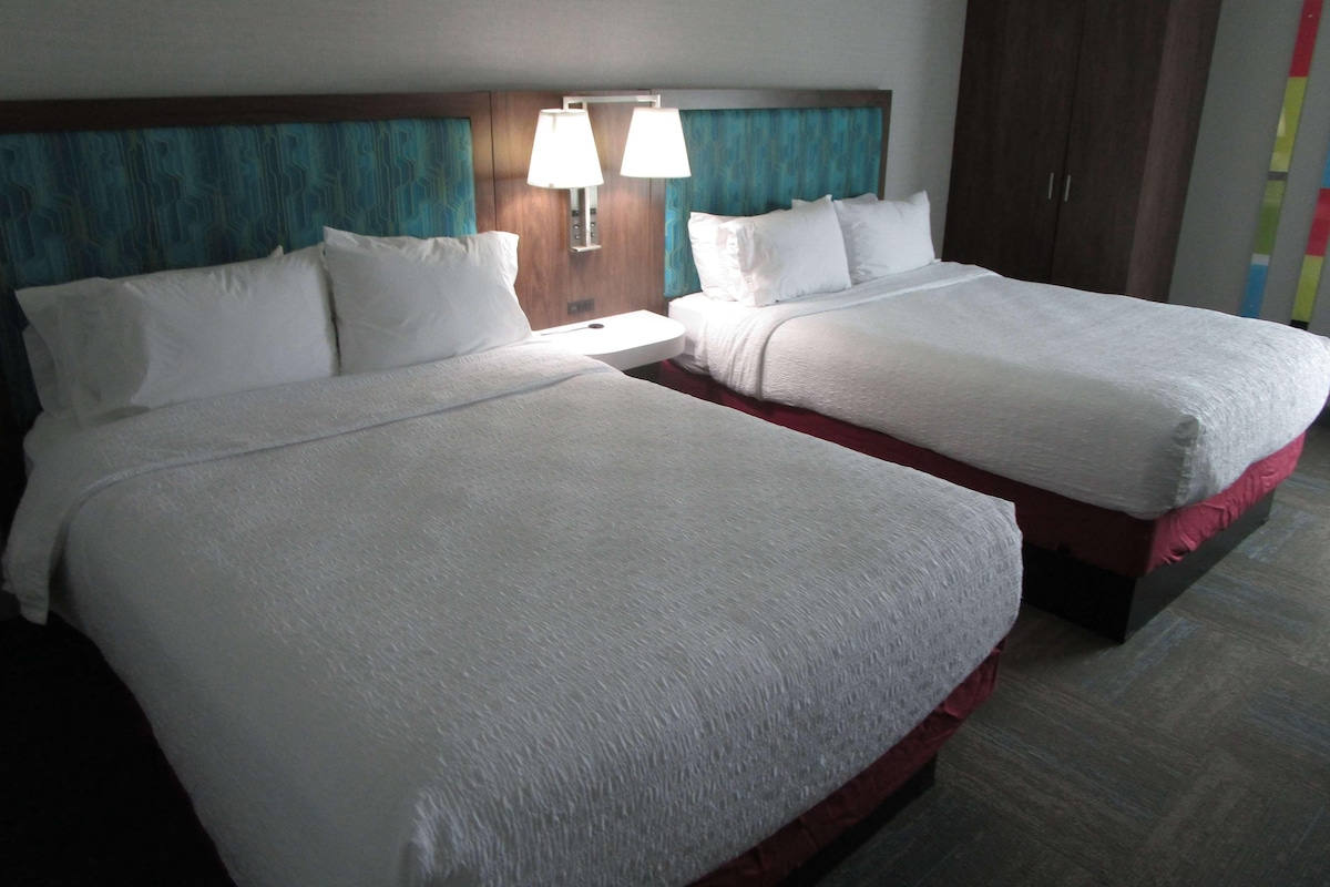 Two beds with white linens, a wooden headboard, and two bedside lamps.