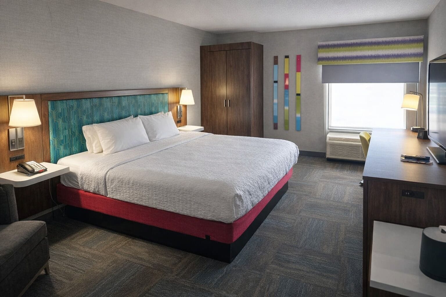 A hotel room with a bed, bedside tables, a desk, a TV, and a window with blinds.