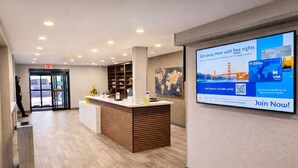 A modern reception area with a wooden reception desk, a digital screen advertising free nights, and a visible exit sign. - Best Western Cy-Fair (Houston)