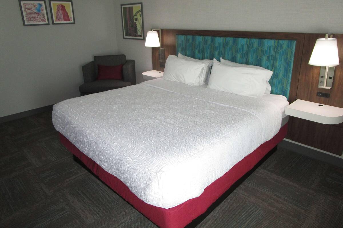 A hotel room with a large bed, two bedside tables, a chair, and artwork on the walls.