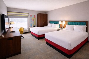 A hotel room with two beds, a desk, a chair, a TV, and a window.