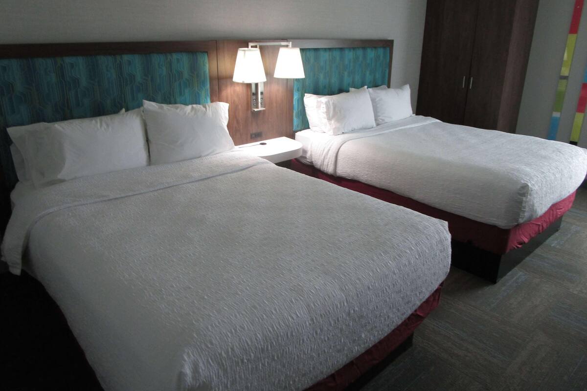 Two beds with white linens, a wooden headboard, and two bedside lamps.