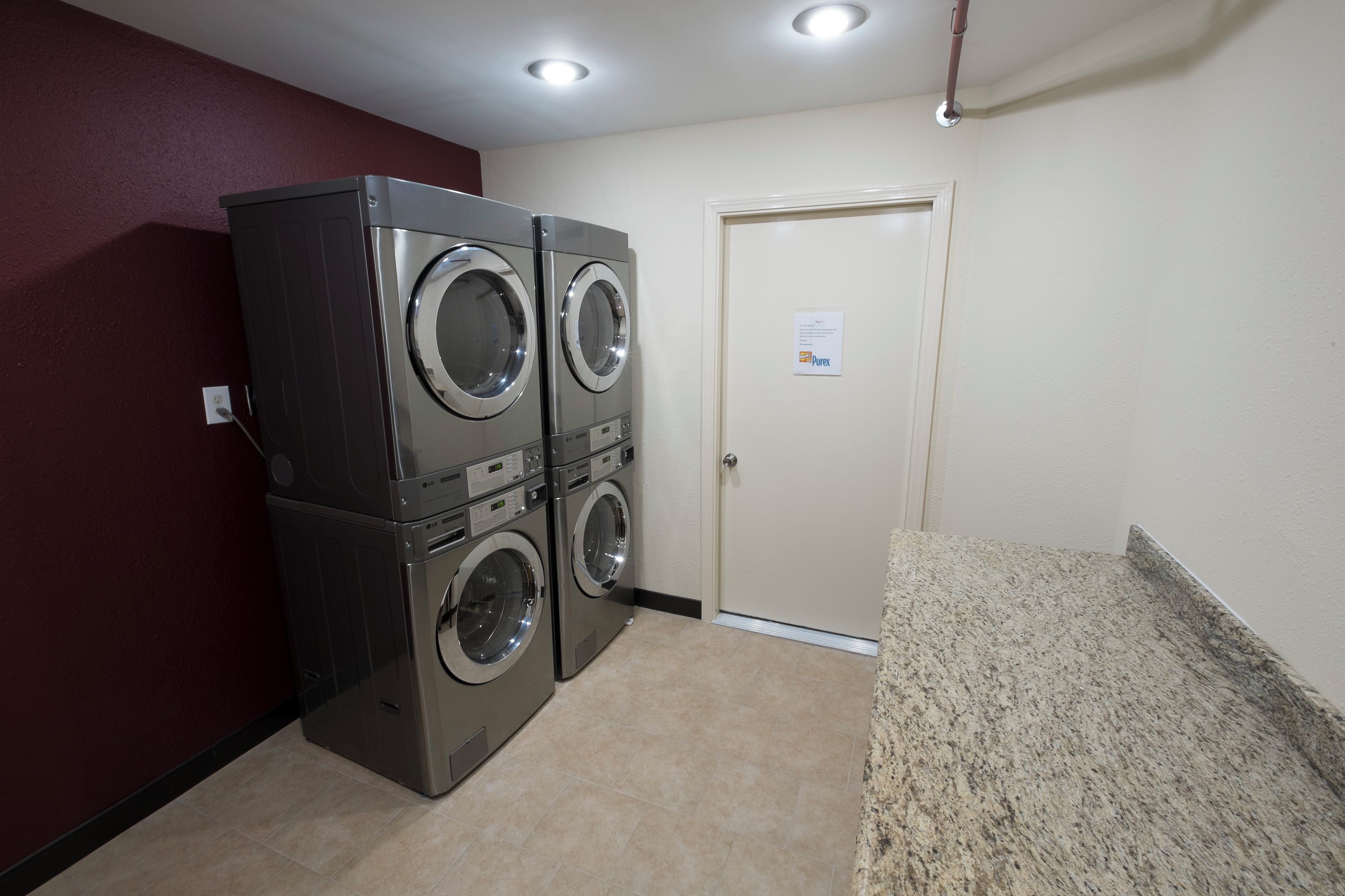 A laundry room with two stacked front-loading washers and dryers, a door with a sign, and a granite countertop.