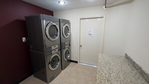 A laundry room with two stacked front-loading washers and dryers, a door with a sign, and a granite countertop. - Red Roof Inn PLUS+ Houston - Energy Corridor (Houston)
