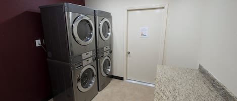 A laundry room with two stacked front-loading washers and dryers, a door with a sign, and a granite countertop.