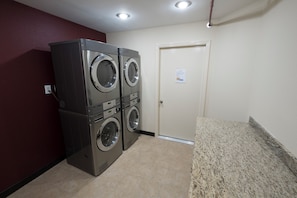 A laundry room with two stacked front-loading washers and dryers, a door with a sign, and a granite countertop. - Red Roof Inn PLUS+ Houston - Energy Corridor (Houston)