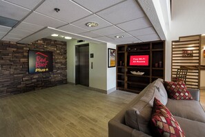 A hotel lobby with a Red Roof Plus sign, an elevator, a free Wi-Fi sign, and a wooden bookshelf. - Red Roof Inn PLUS+ Houston - Energy Corridor (Houston)