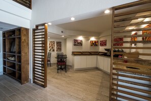 A modern kitchen with wooden cabinets, a dining area with chairs, and artwork on the walls. - Red Roof Inn PLUS+ Houston - Energy Corridor (Houston)