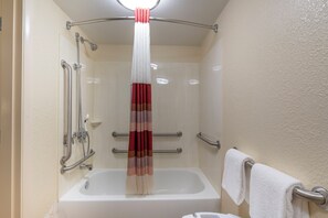 A bathroom with a bathtub, a shower with grab bars, and a towel rack.