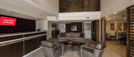 A hotel lobby with a reception desk, a seating area with sofas and chairs, and a high ceiling with wooden slats.