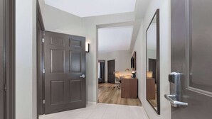 Un couloir avec une porte en bois foncé, un sol carrelé de couleur claire et un miroir accroché au mur.