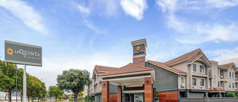 A hotel with a covered entrance, a sign with a sun logo, and a tiled roof.