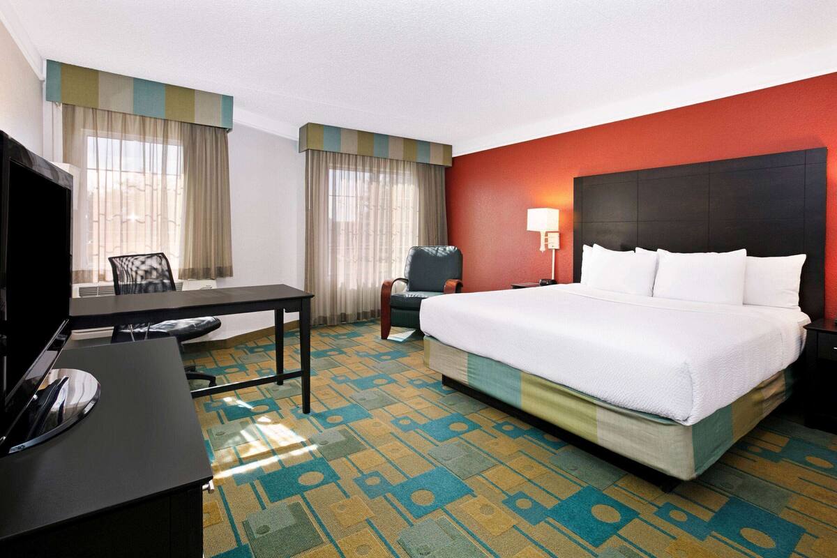 Habitación de hotel con cama, escritorio, silla, televisor y lámpara.