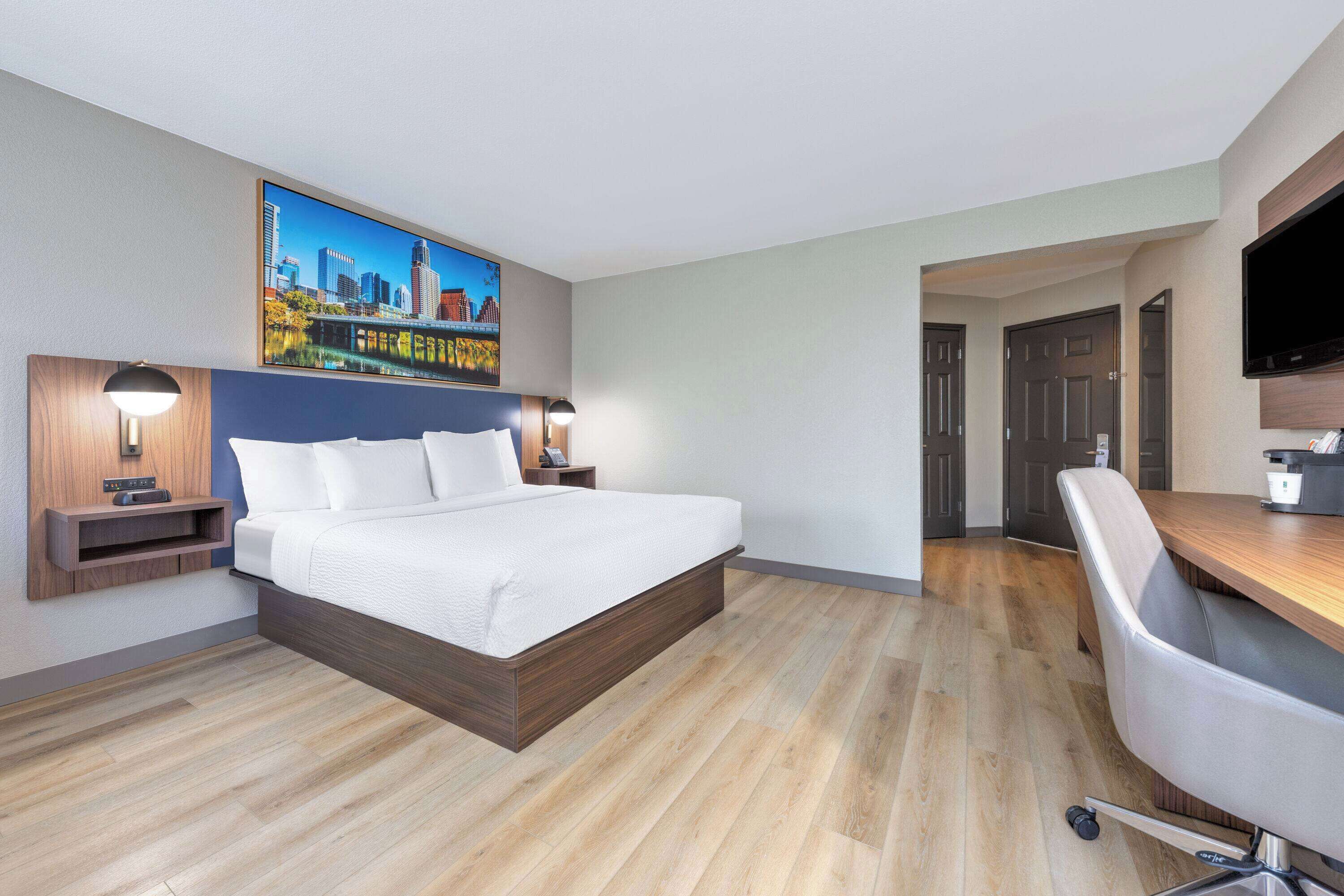 Ein Hotelzimmer mit Bett, Nachttischen, Schreibtisch, Stuhl und Fernseher.