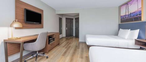 A hotel room with a wooden desk, a television, a white sofa, and a painting of a bridge.