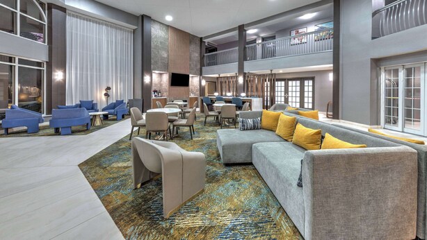 Un hall d’entrée spacieux, avec un canapé gris, des fauteuils bleus et une moquette à motifs.
