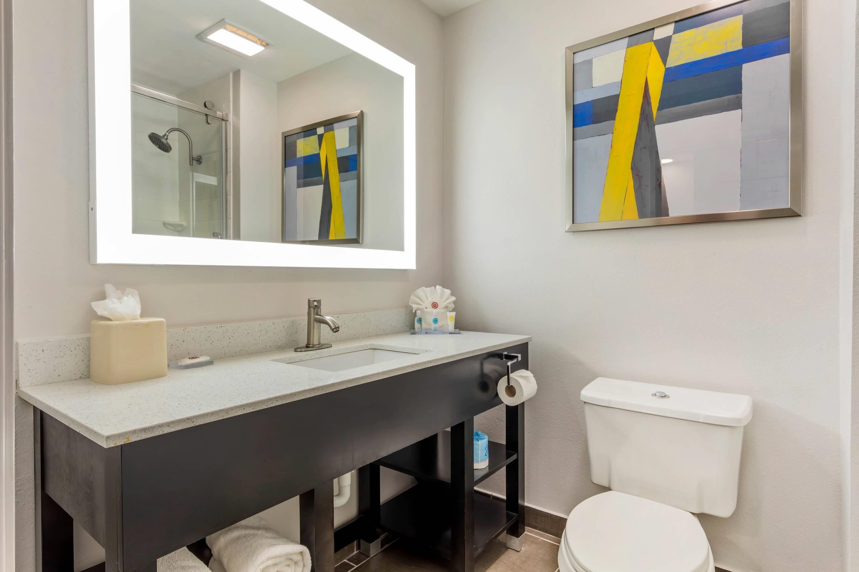 A modern bathroom with a large mirror, a sink, a toilet, and a shower.